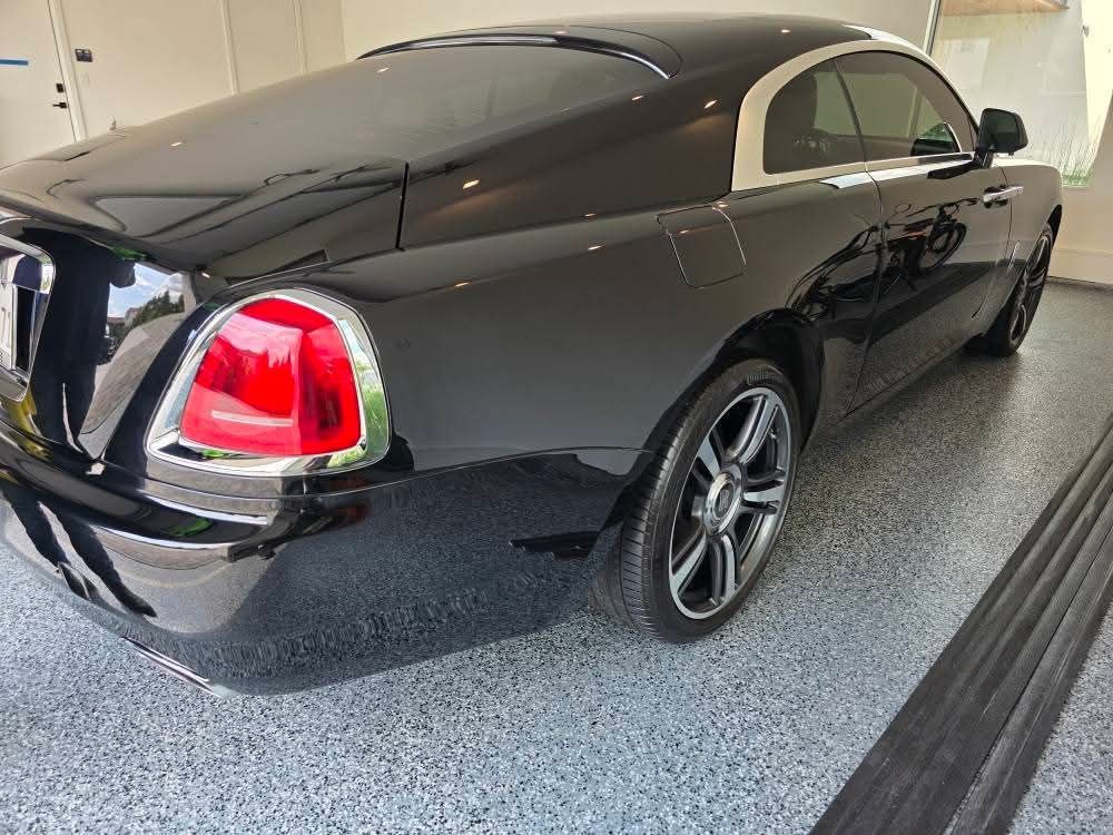 Black luxury coupe parked in a garage, rear three-quarter view with red taillights and tinted windows