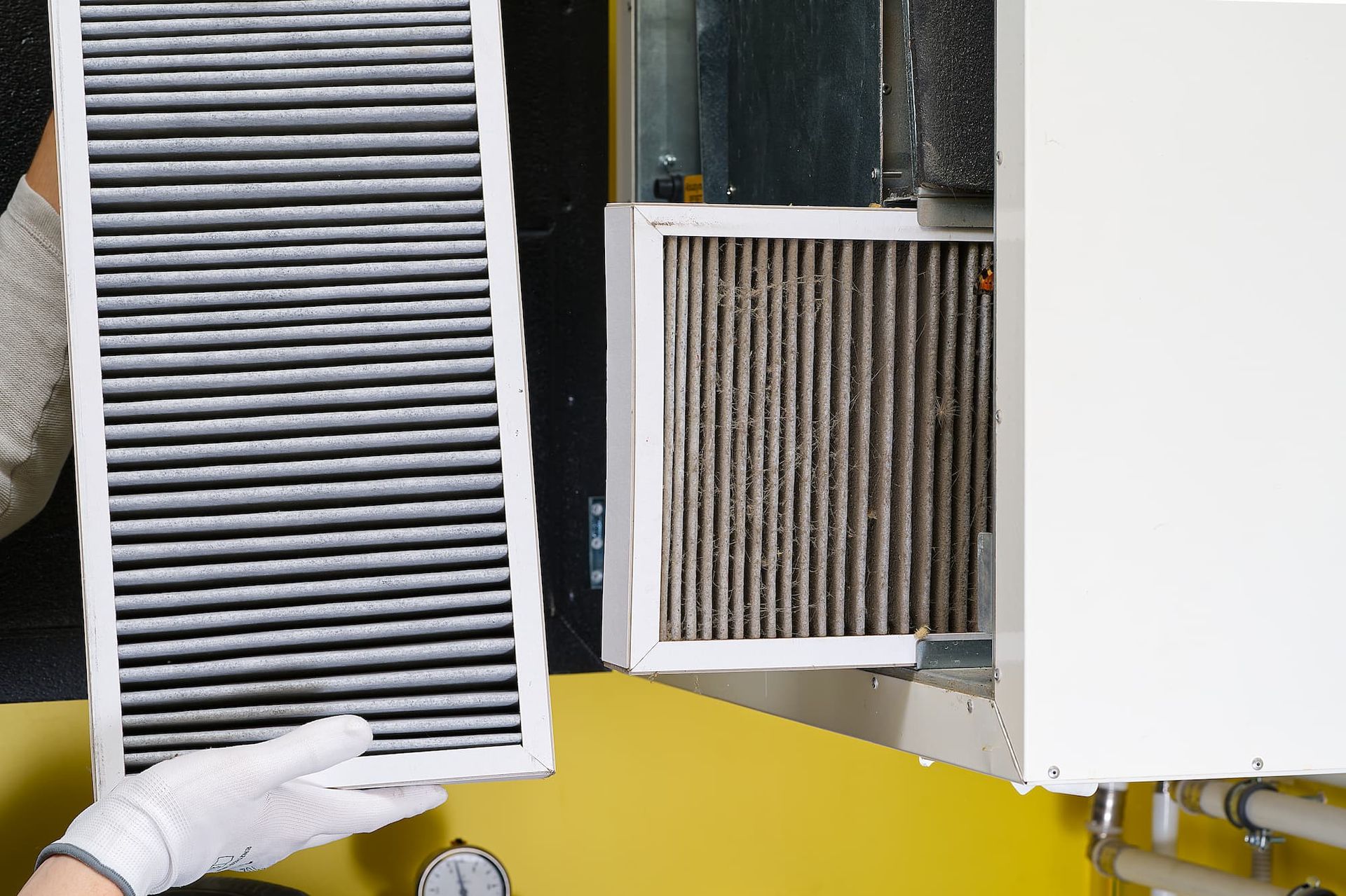 Gloved hand holding a dirty HVAC air filter beside a clean replacement filter in a maintenance setting