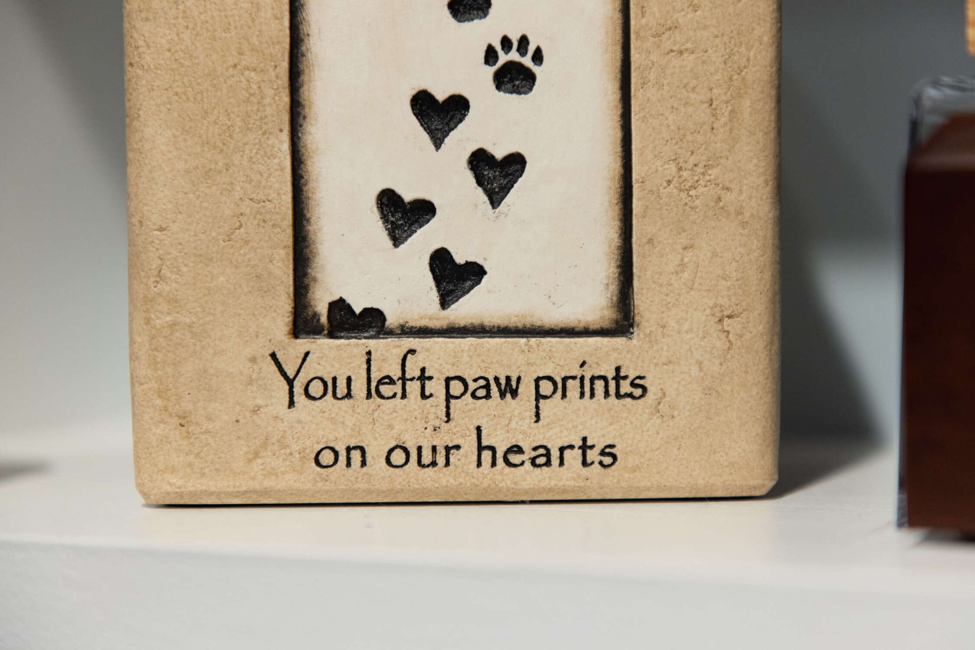 Small beige decorative plaque with black paw prints and hearts, reading “You left paw prints on our hearts”