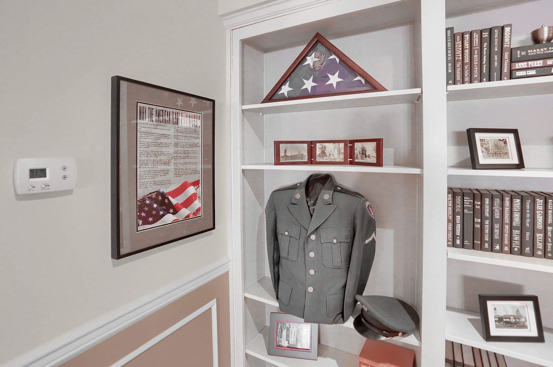 Framed military display with folded American flag, uniform jacket, medals, and bookshelves in a home office