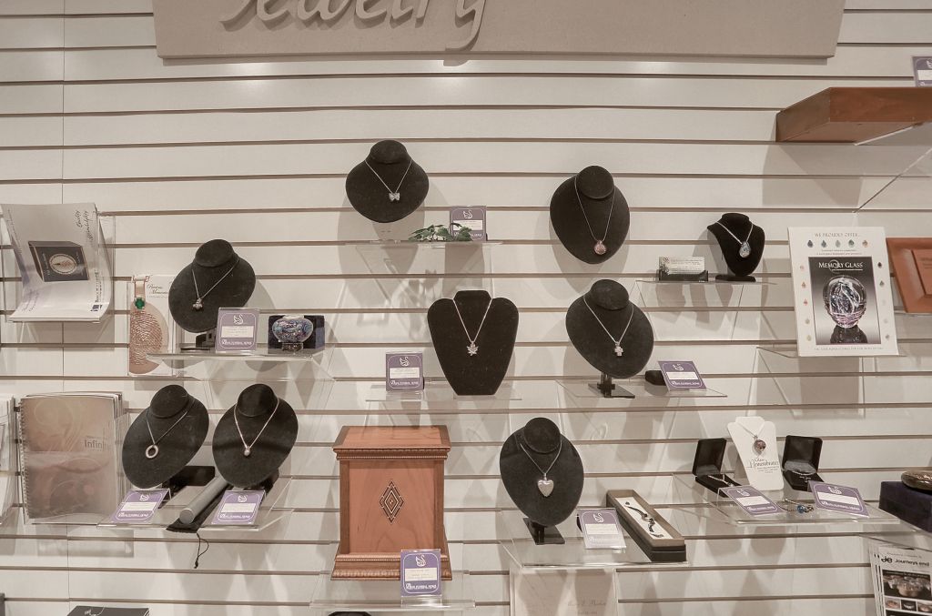 Jewelry display with black necklace busts, watches, and a few framed photos on white slatwall shelves