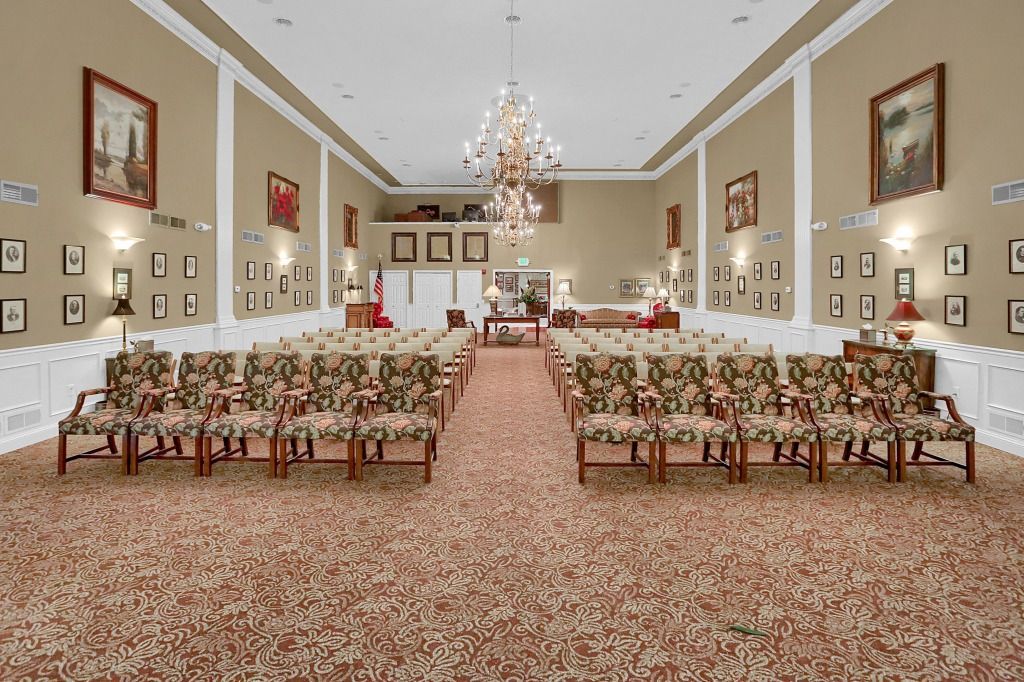 Elegant banquet hall with rows of floral chairs, pink carpet, chandeliers, and framed wall art