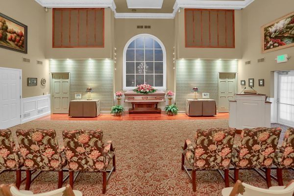 Elegant chapel interior with floral carpet, arched window, and front altar decorated with pink flowers