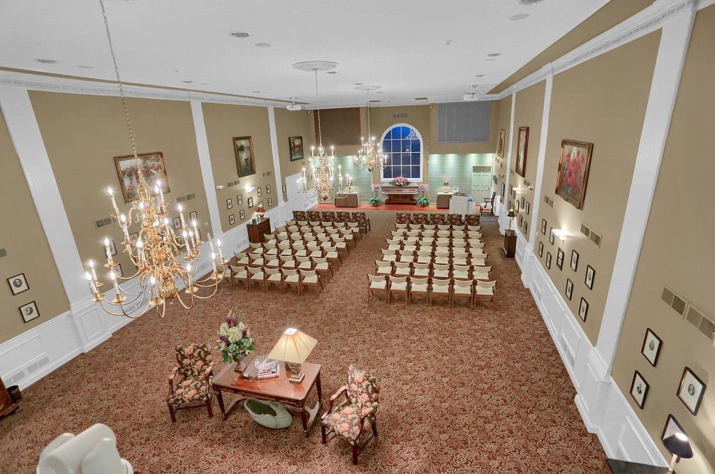 Empty hall with rows of chairs, a head table, and chandeliers on carpeted floor