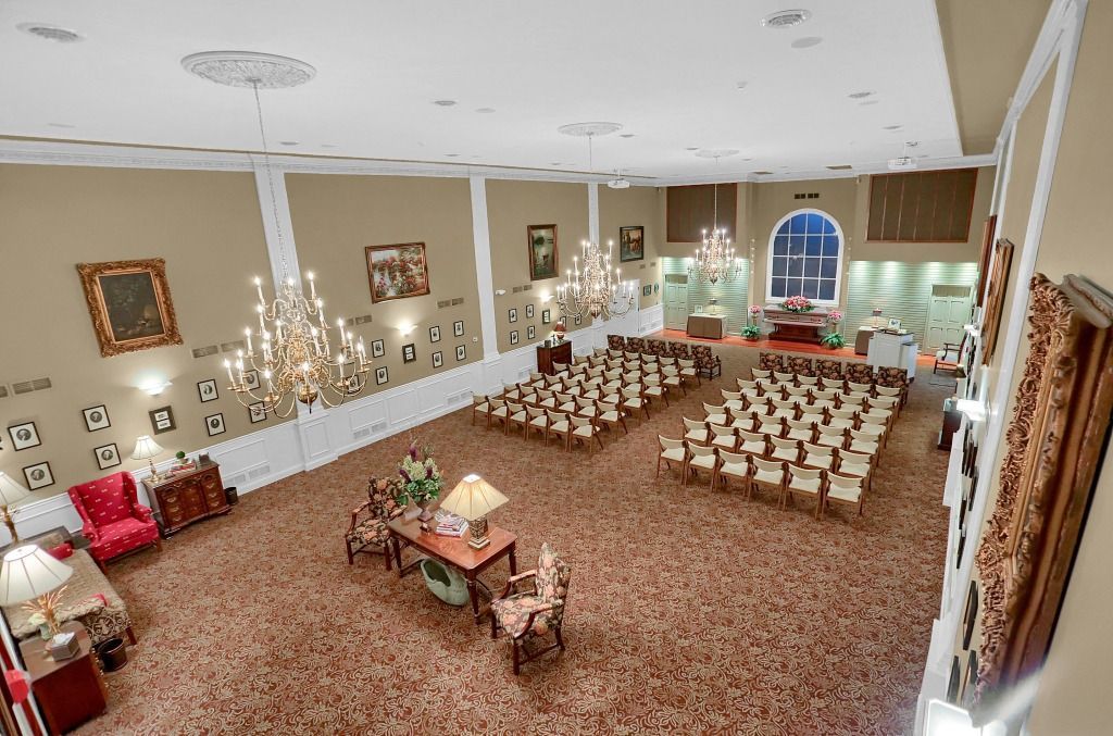 Elegant banquet hall with chandeliers, rows of chairs, and a decorated table near large windows