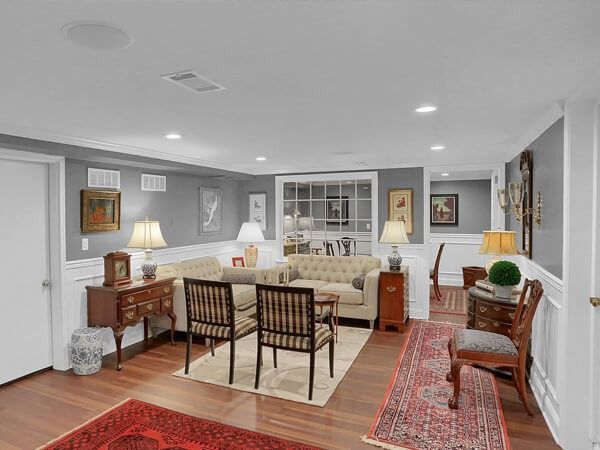 Bright living room with cream seating, wooden chairs, red rug, and framed art on gray walls