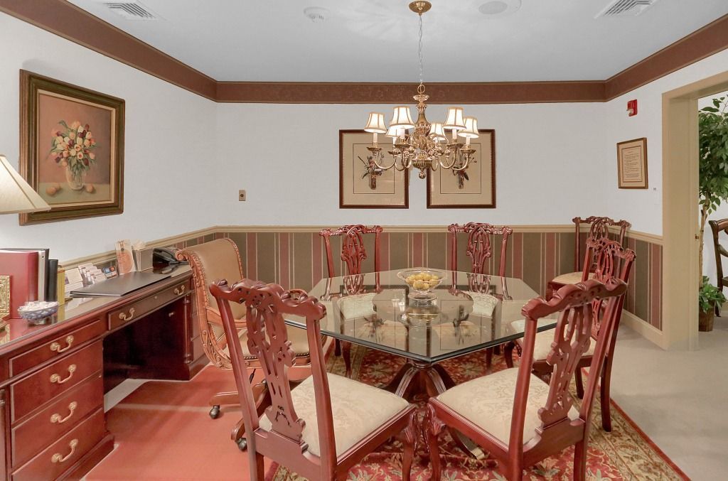 Elegant dining room with chandelier, glass table, ornate red chairs, and framed wall art
