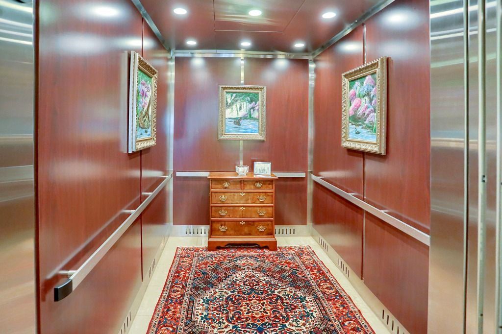 Empty elevator with red walls, framed art, and a patterned rug leading to a wooden cabinet.