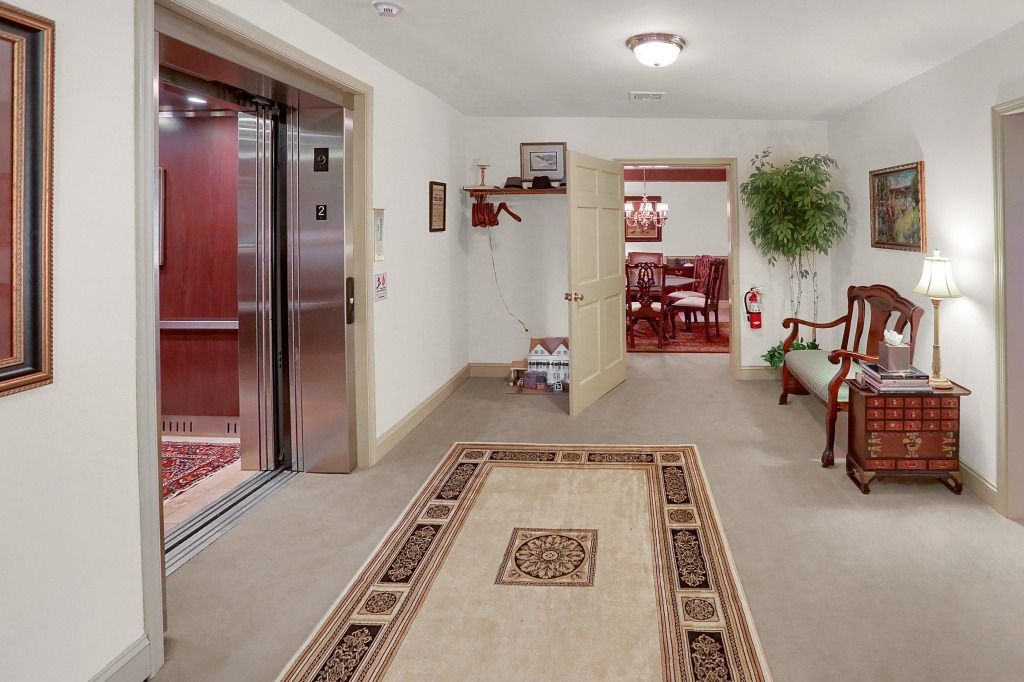 Bright hallway with beige carpet, rugs, open elevator, and red dining room visible ahead