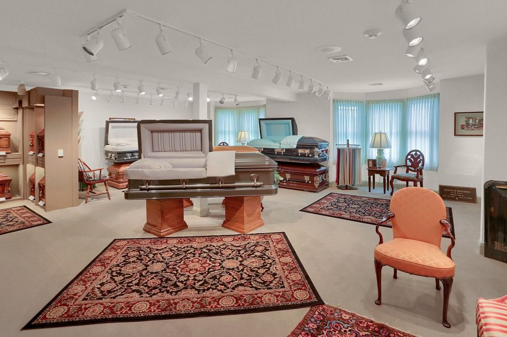 Bright white showroom with a casket on display, patterned rugs, chairs, and track lighting.