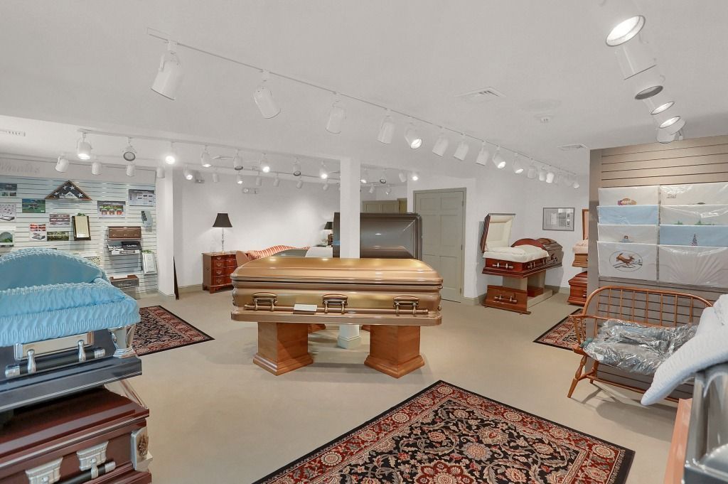 Bright, modern showroom with a large wooden table, patterned rugs, and shelves of home decor items.
