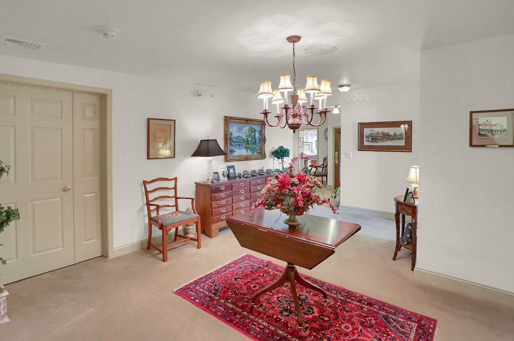 Elegant dining room with chandelier, red rug, wooden table, sideboard, and framed wall art.