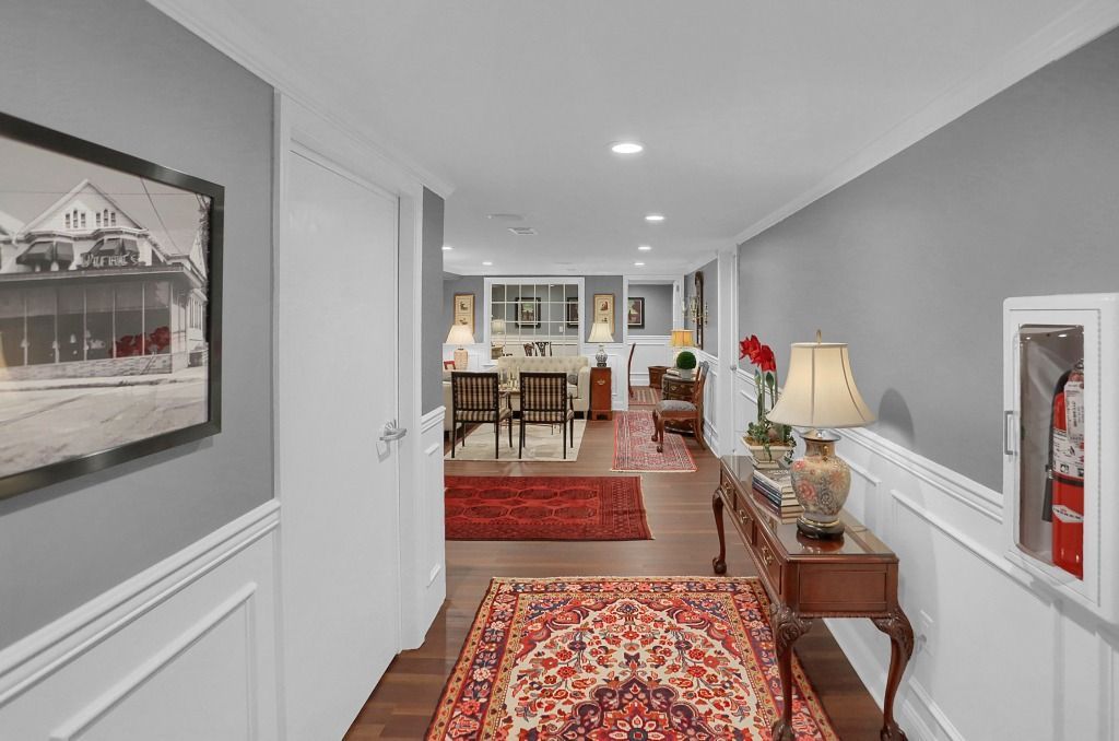 Narrow hallway with red patterned runner, white walls, framed art, and a glimpse of a dining room ahead
