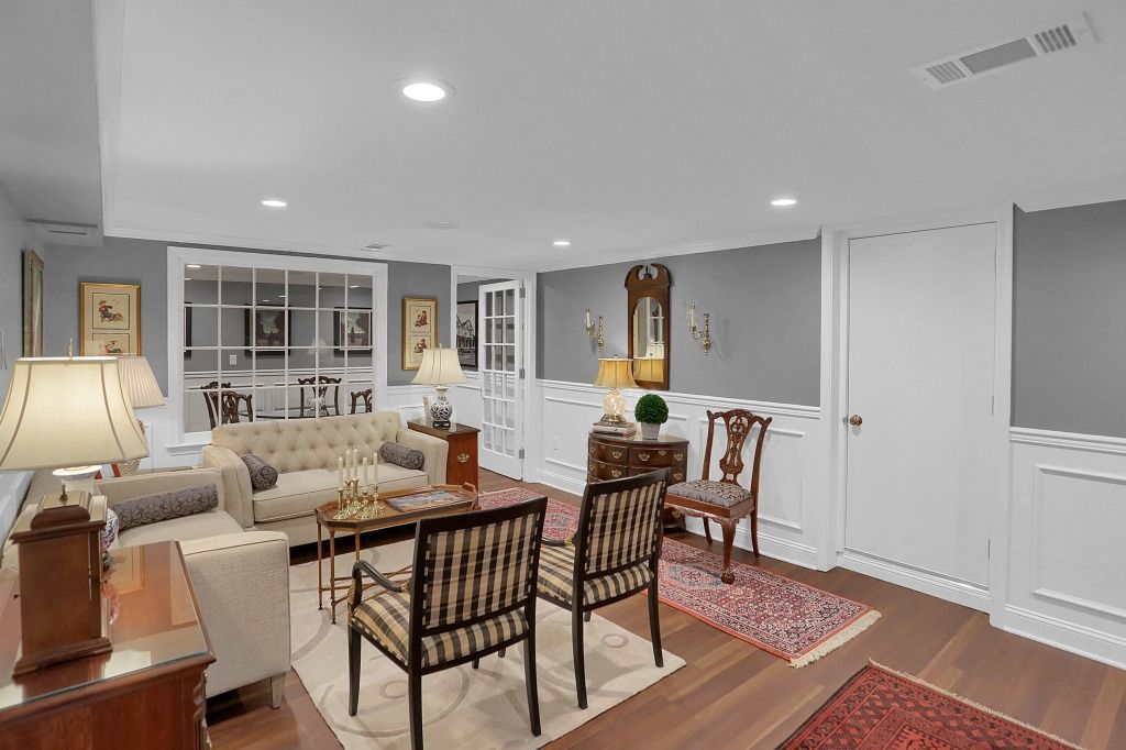Elegant living and dining room with cream sofas, wooden chairs, red rug, and recessed ceiling lights
