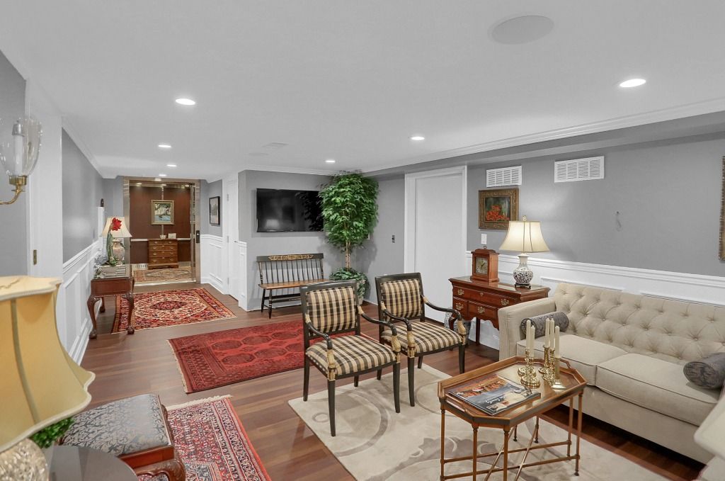 Bright living room with cream sofa, striped chairs, rugs, table lamps, and a hallway in the back