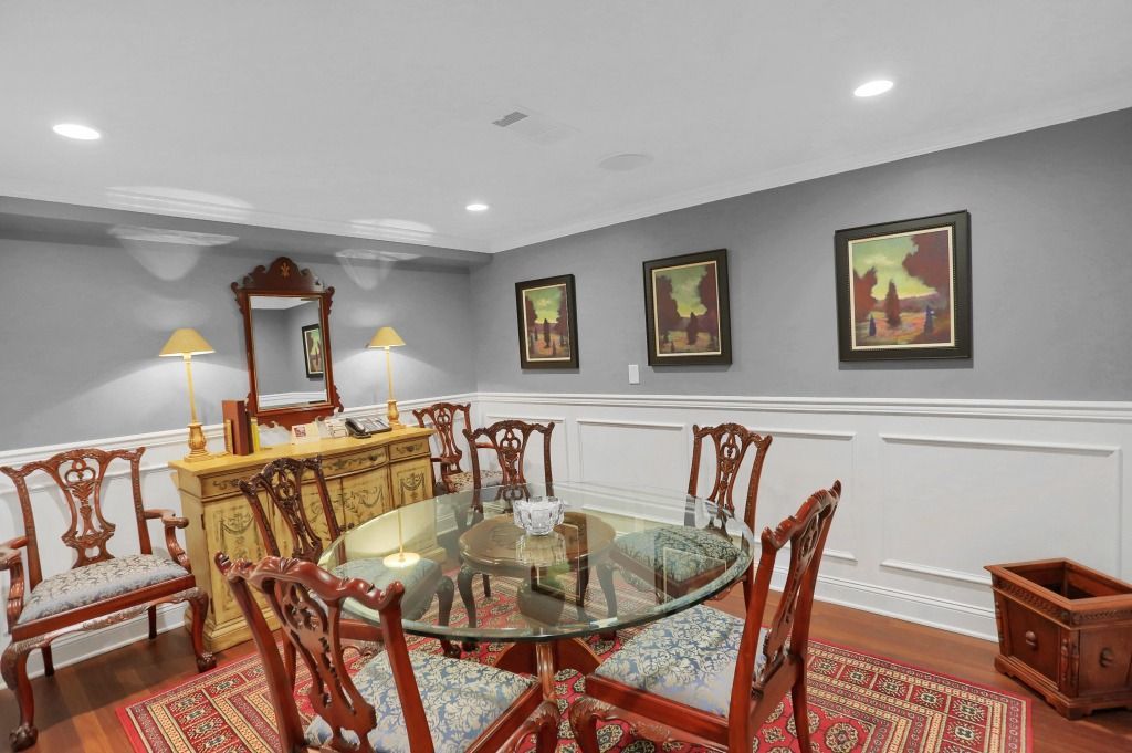 Elegant dining room with glass table, ornate chairs, patterned rug, and framed wall art.