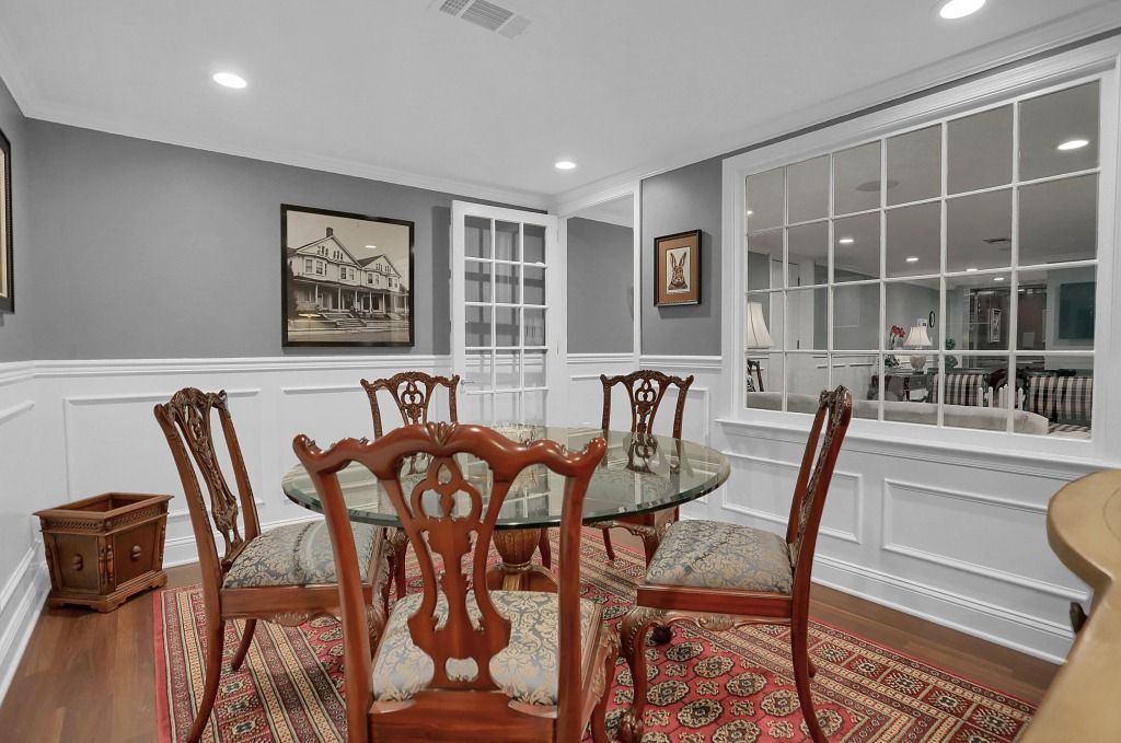 Elegant dining room with glass table, wooden chairs, red rug, gray walls, and large window seat area