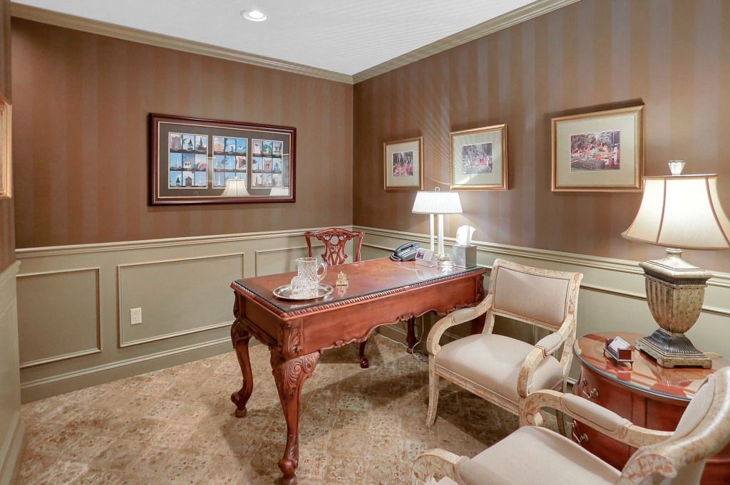 Elegant wood-paneled office with a carved desk, cream chairs, framed art, and a lamp on the side table