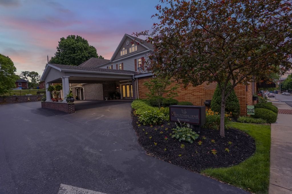 Suburban house entrance with covered driveway, brick facade, landscaping, and a dusk sky