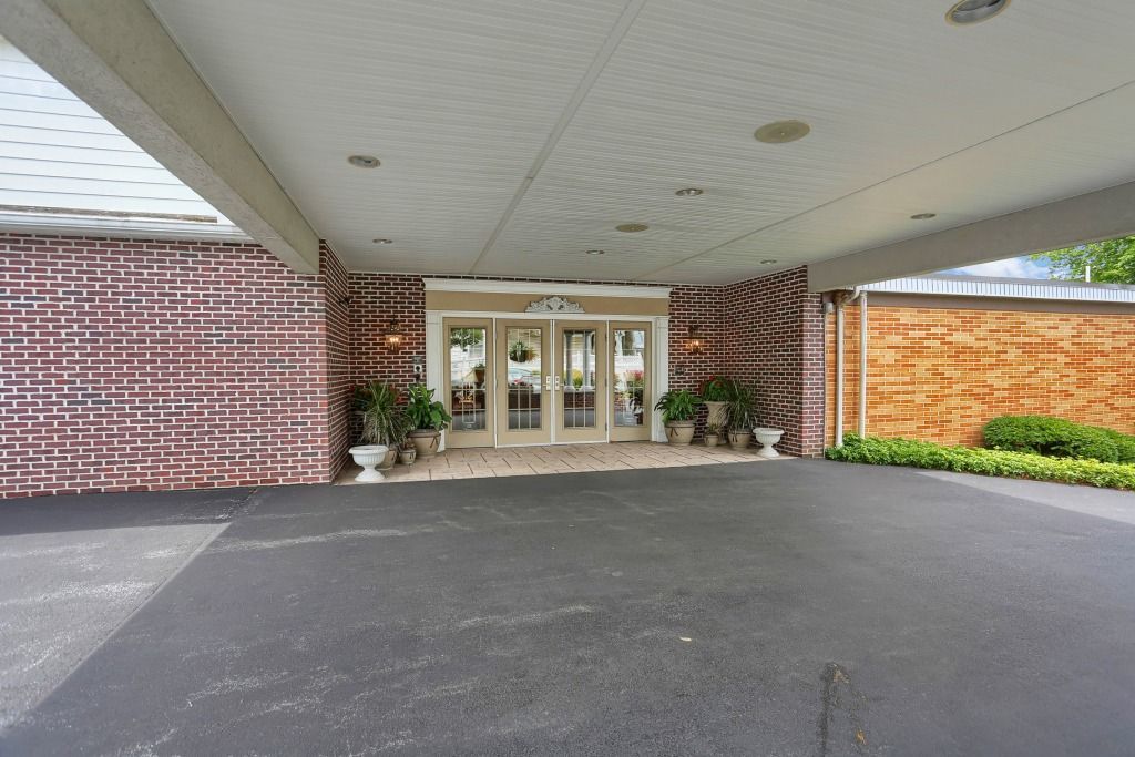 Covered driveway entrance with glass doors, brick walls, and landscaped planters