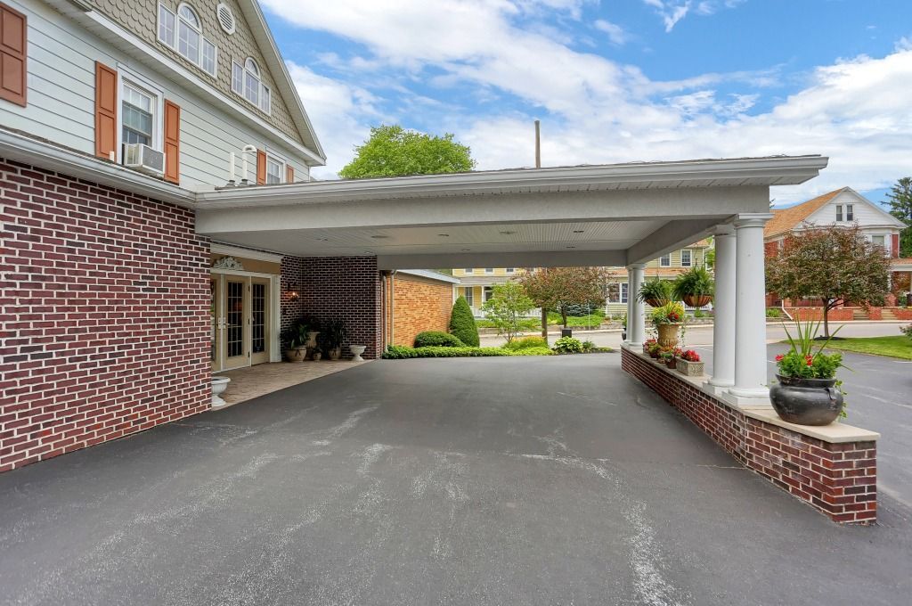 Covered brick driveway entrance beside a house with a white canopy and potted plants