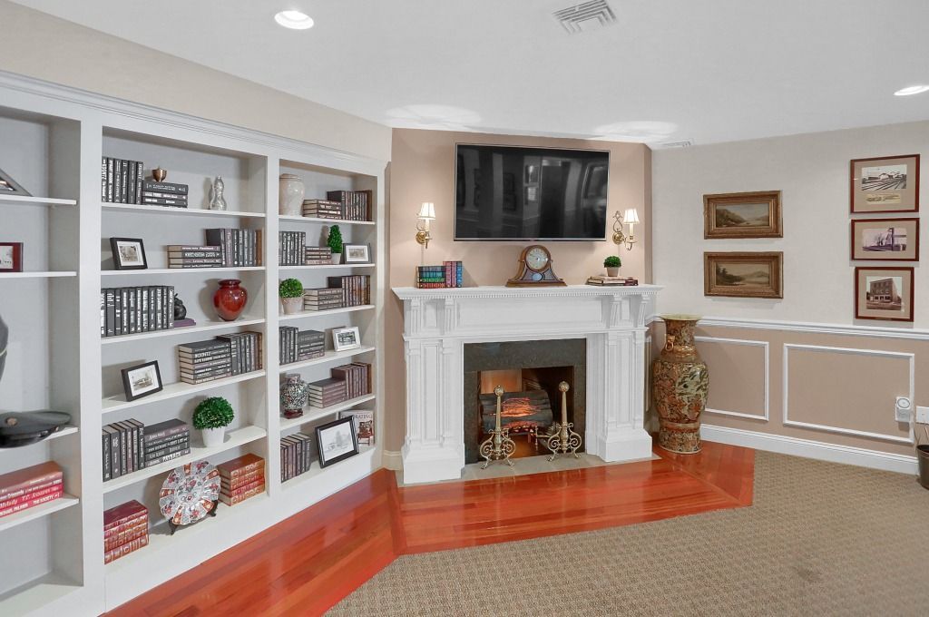 Bright living room with white built-in bookshelves, fireplace, wall-mounted TV, and beige carpet