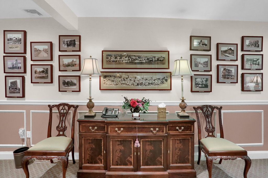 Elegant hallway with framed artwork, a wooden console table, and two upholstered chairs against a pale wall.