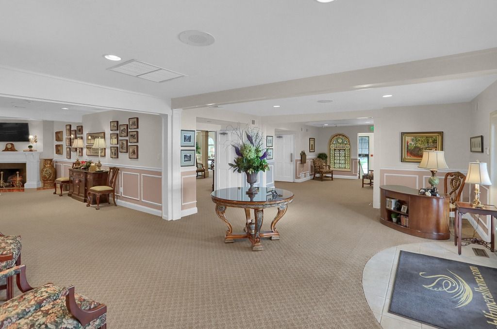 Spacious carpeted lounge with seating, tables, artwork, and a fireplace in a bright, open interior