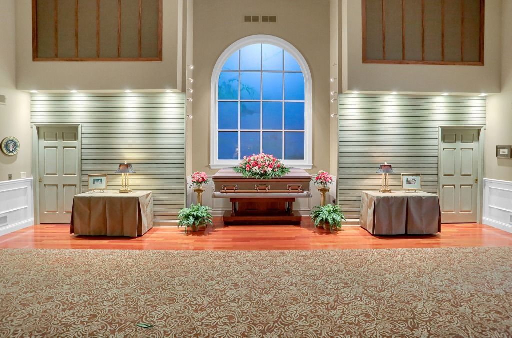 Elegant hall with central arched window, altar table, floral arrangements, and two draped display tables