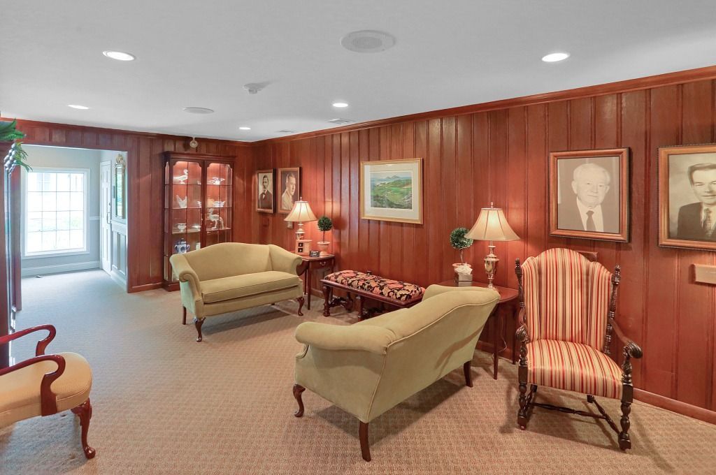 Elegant wood-paneled lounge with beige and striped chairs, lamps, and framed artwork.