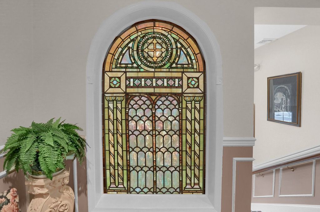 Decorative stained-glass window in a hallway beside a potted fern and staircase opening