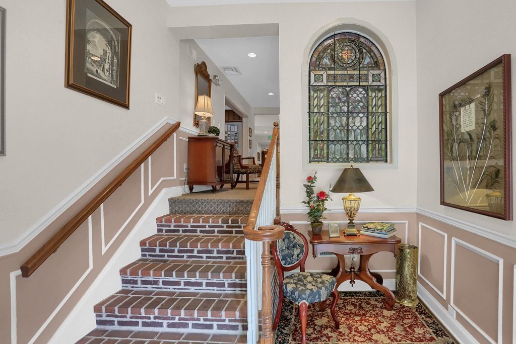 Elegant foyer with carpeted staircase, stained-glass window, and decorative table with lamp and flowers
