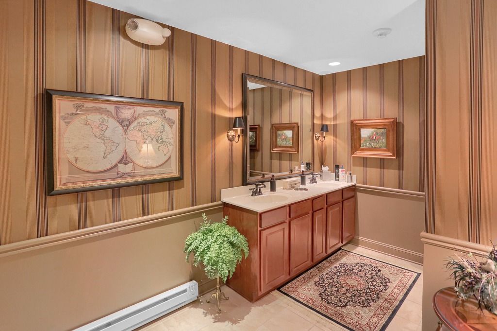Small vintage bathroom with wood-paneled walls, a vanity sink, framed art, rug, and potted plant.