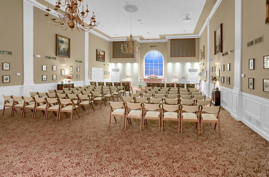 Elegant hall with rows of white chairs, chandeliers, and a large arched window.