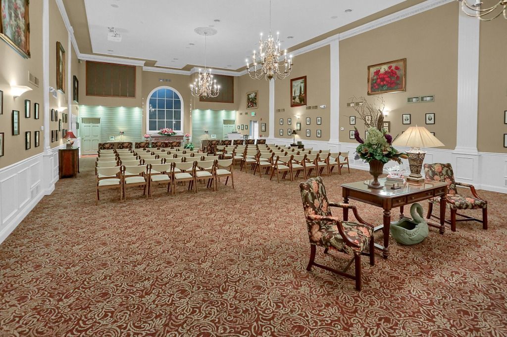 Elegant banquet hall with rows of chairs, chandeliers, and a set table in the foreground