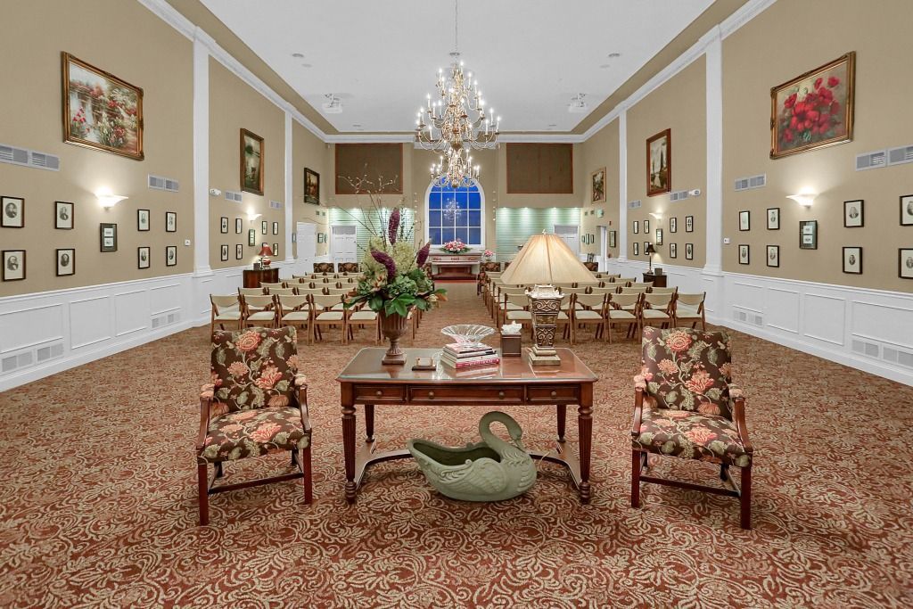 Elegant formal dining room with long table, chandelier, patterned carpet, and wall art.