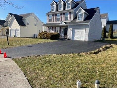 Suburban house with a freshly paved black driveway and two orange cones near the sidewalk.