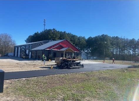 Roadside building with red roof, people nearby, and a brush pile in front under a clear blue sky