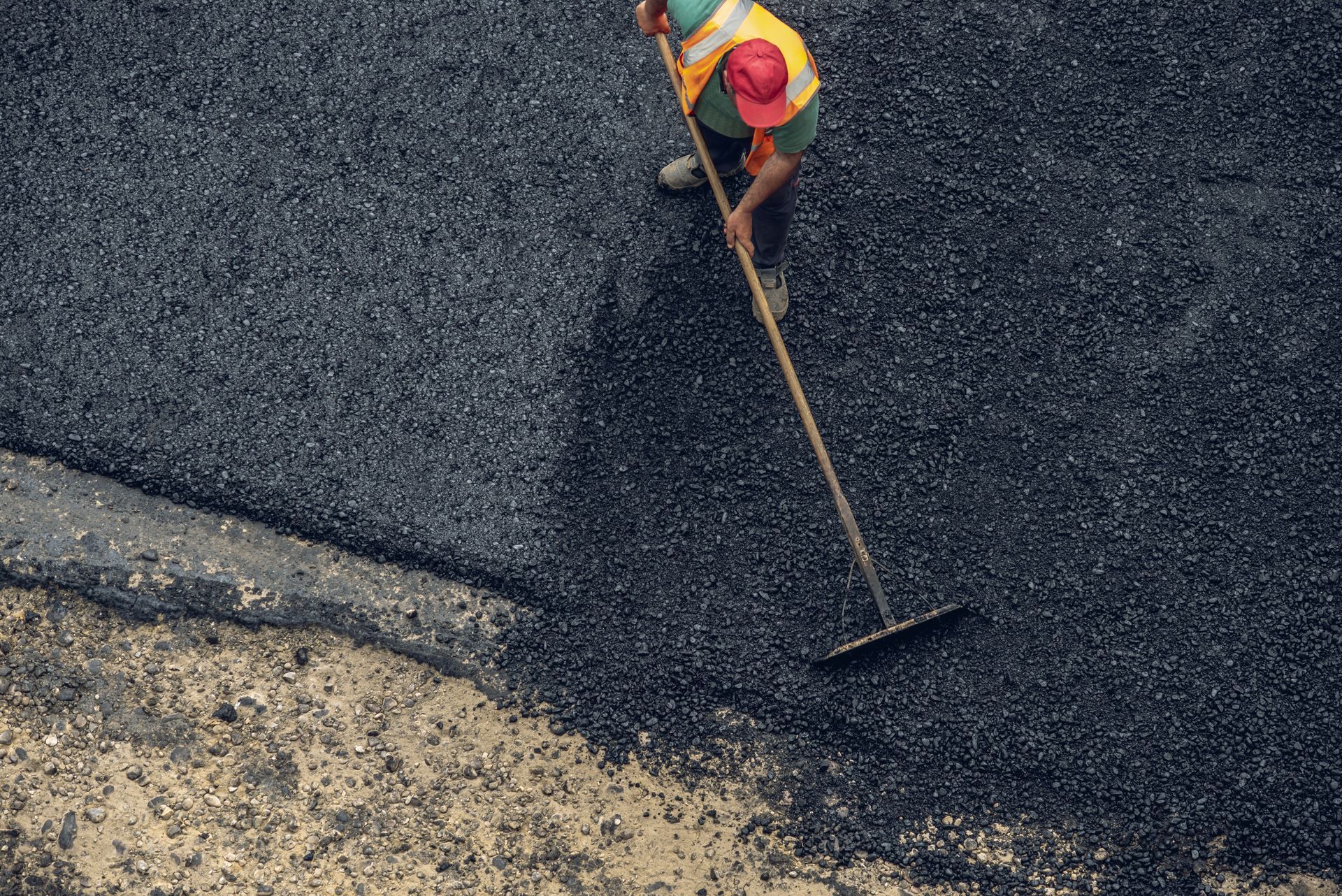 Worker spreading fresh asphalt with a rake on a road surface