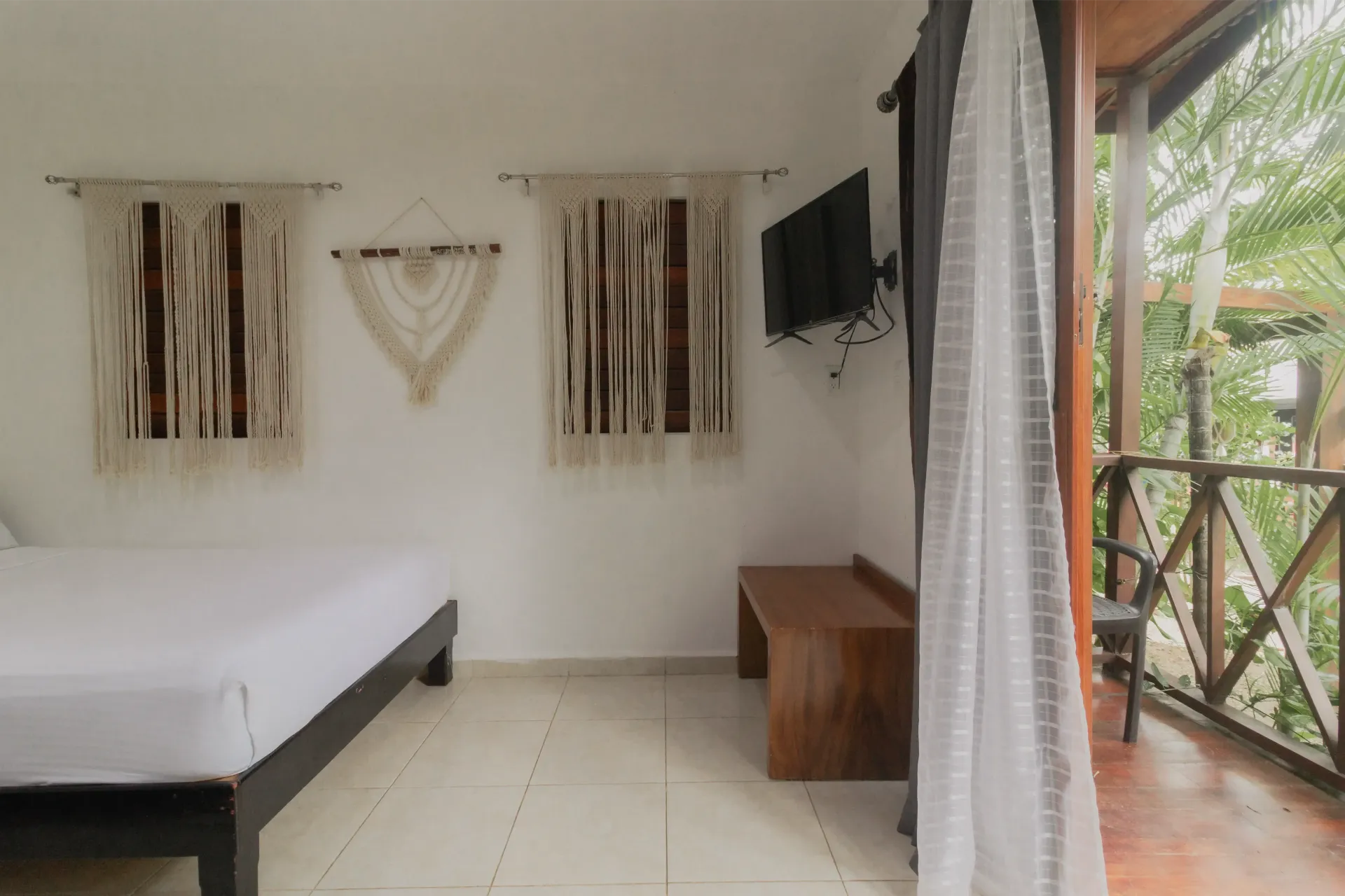 Habitación luminosa con cama, banco de madera, decoración de pared y puertas correderas que dan a un balcón ajardinado.