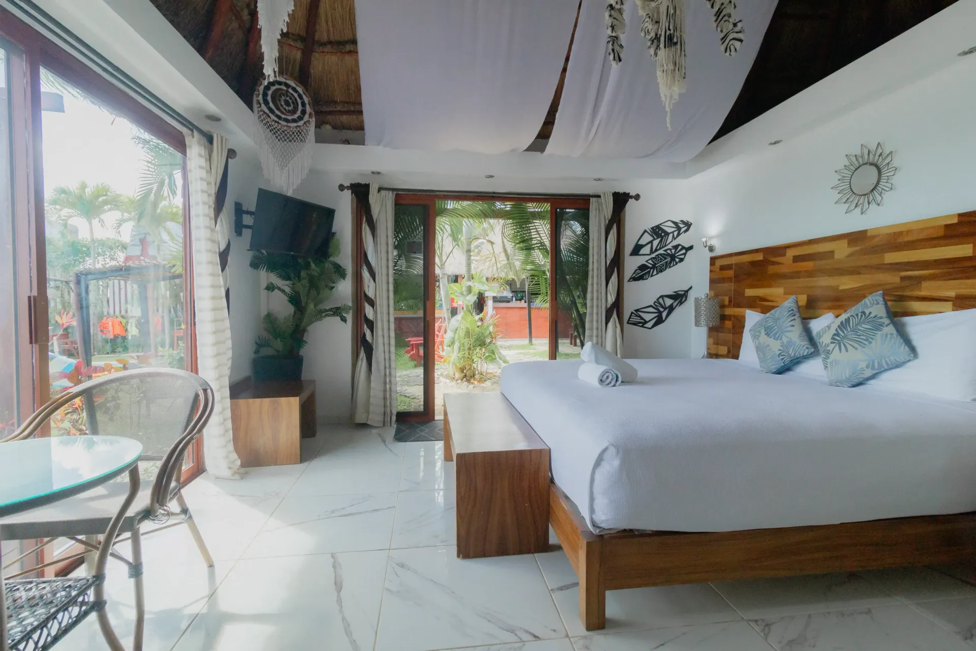 Habitación luminosa de estilo bohemio con ropa de cama blanca, detalles en madera, plantas y puertas corredizas.