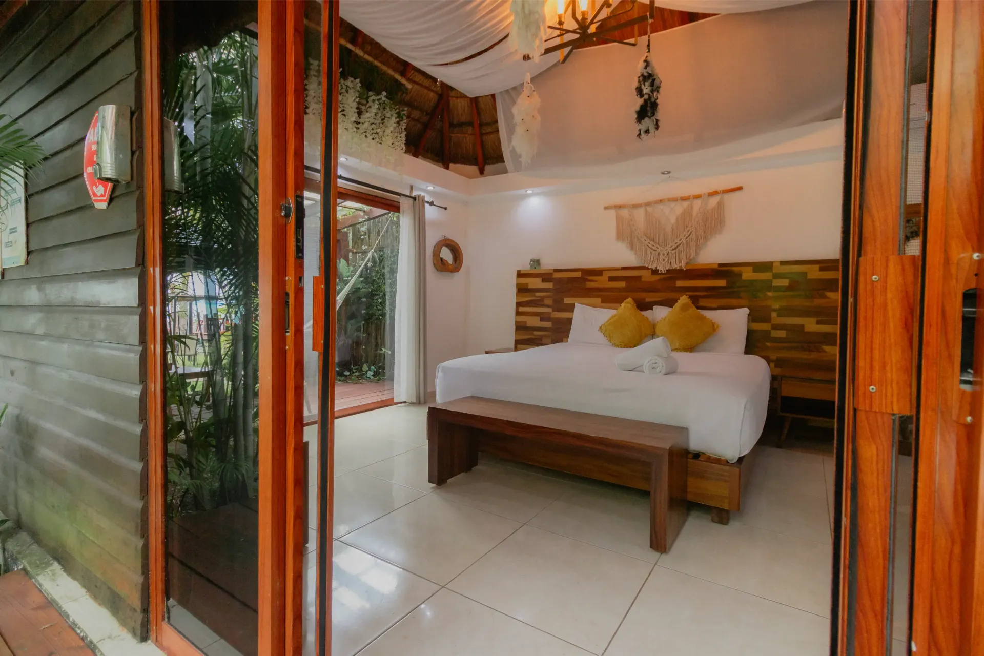 Dormitorio moderno con cama blanca, detalles en madera y puertas de cristal abiertas con vistas a un exuberante paisaje