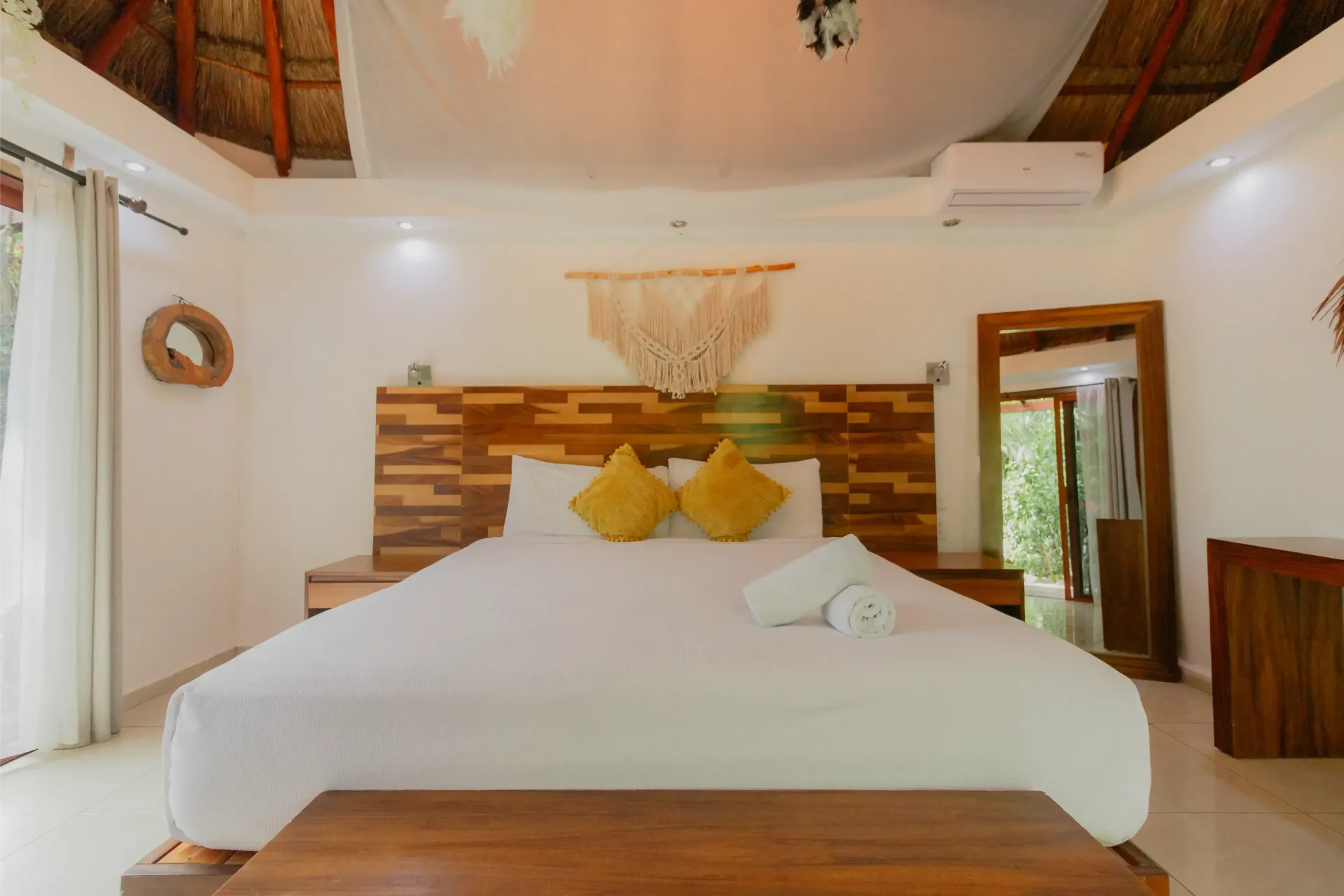 Habitación tropical luminosa con ropa de cama blanca, cabecero de madera y detalles en madera cálida.