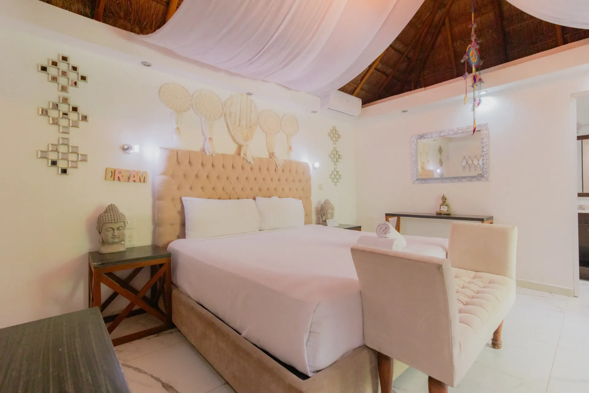 Habitación luminosa y espaciosa con cama blanca, cabecero tallado y decoración de techo tejida.