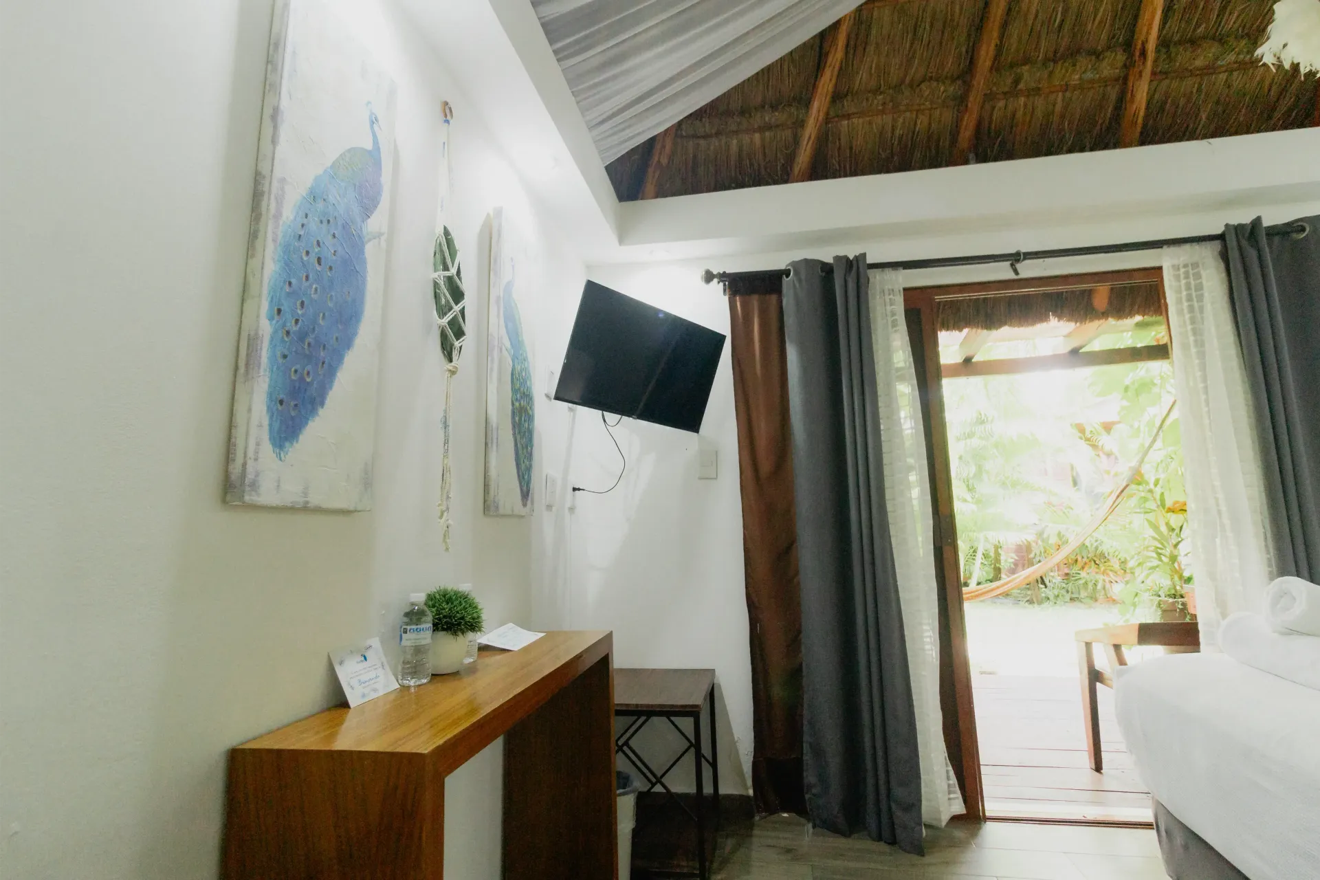 Dormitorio moderno con televisor montado en la pared, cómoda de madera y puerta de balcón abierta con cortinas.