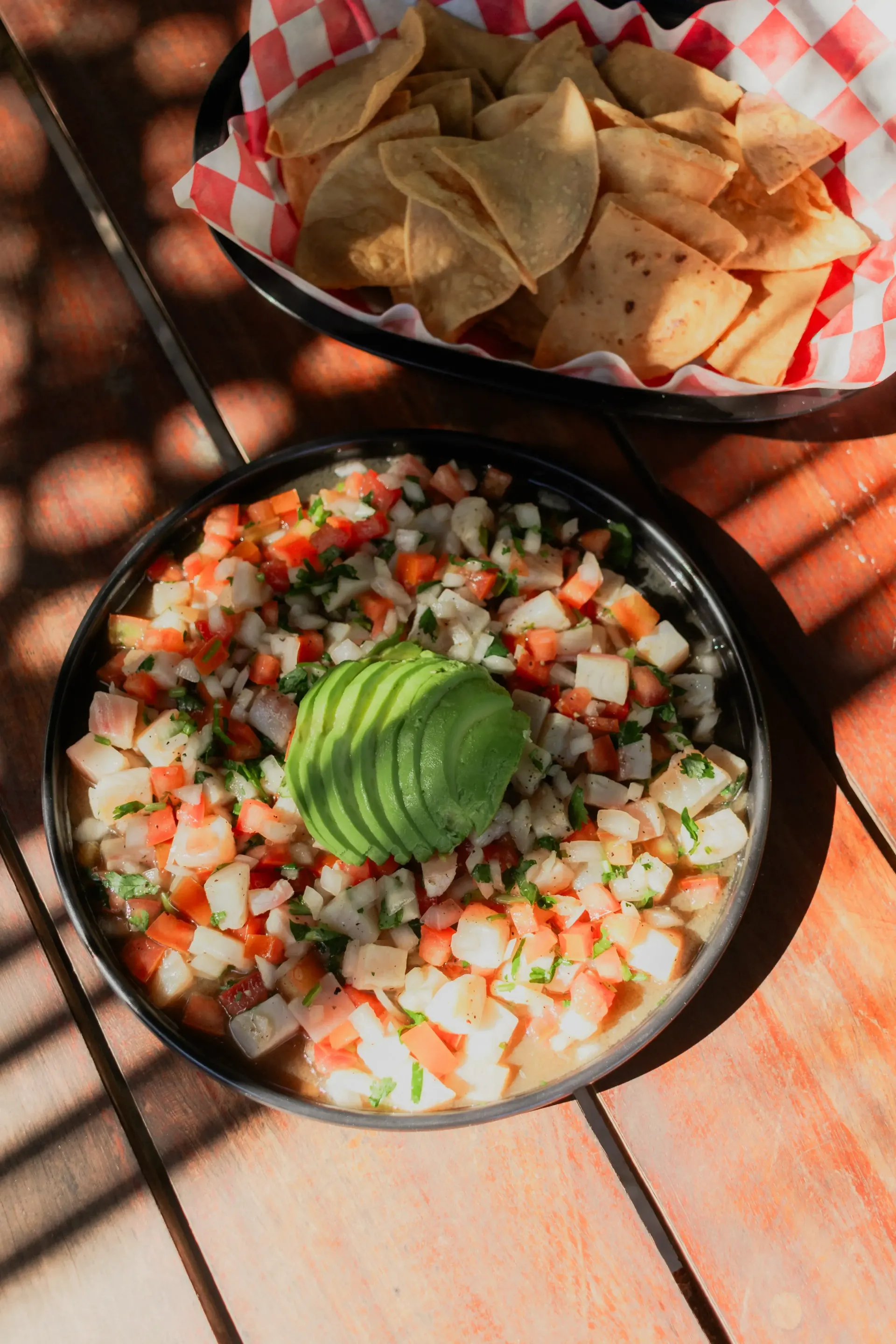 Dos cuencos de salsa y totopos sobre una mesa de madera, coronados con rodajas de aguacate.