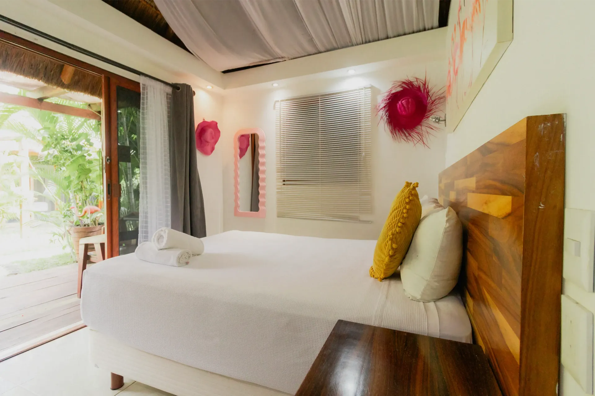 Habitación luminosa con una cama blanca bien hecha, cabecero de madera y ventana abierta con vistas a la vegetación.