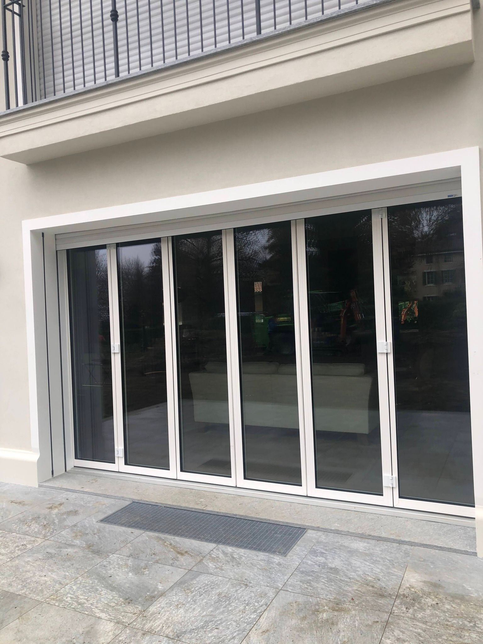 Porte pieghevoli in vetro bianco su un edificio beige con una piccola grata metallica sulla parte anteriore.