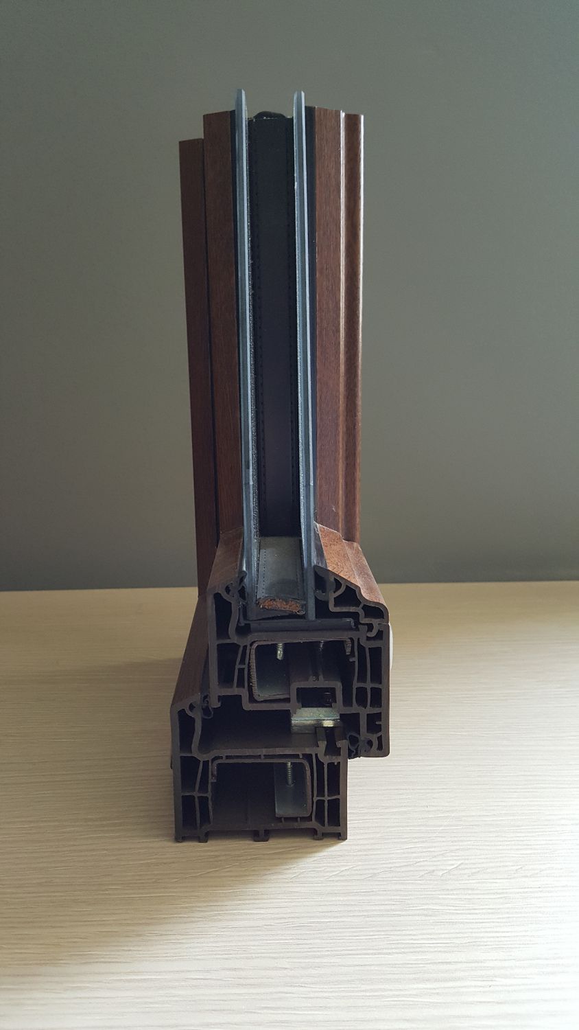 Sezione trasversale di un telaio di finestra in PVC marrone con vetro doppio, che mostra le camere interne e le guarnizioni.