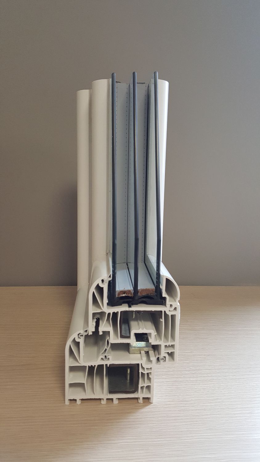 Sezione trasversale di un telaio di finestra bianco a più vetri, che mostra gli strati di vetro e la struttura interna, appoggiato su una superficie di legno.